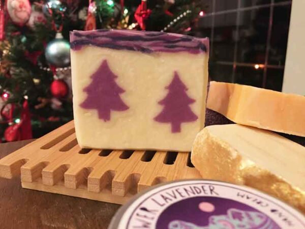 A Lavender soap with a purple Christmas tree design displayed with a Christmas tree and other Gower Lavender soaps