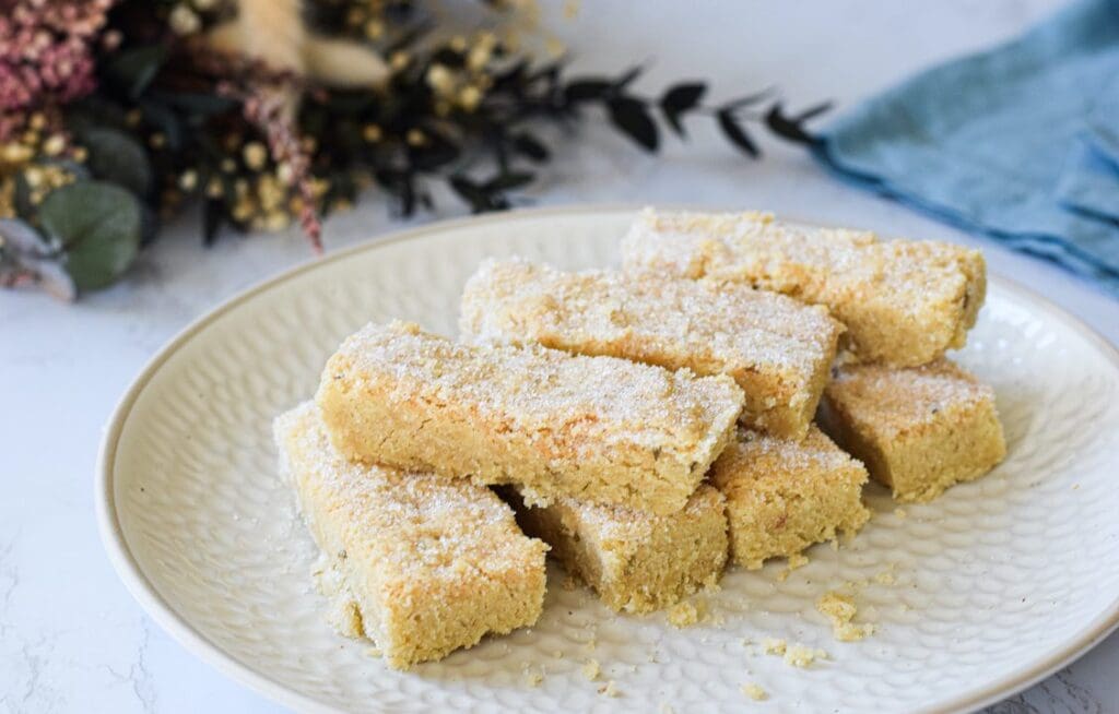 Lavender shortbread biscuits displayed on a white plate and dusted with icing sugar, with green foliage and a pale blue napkin