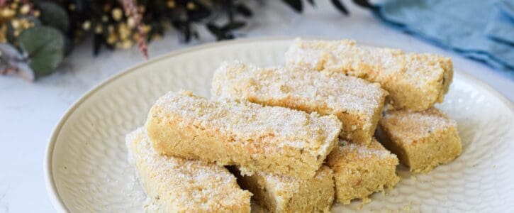 Lavender shortbread biscuits displayed on a white plate and dusted with icing sugar, with green foliage and a pale blue napkin