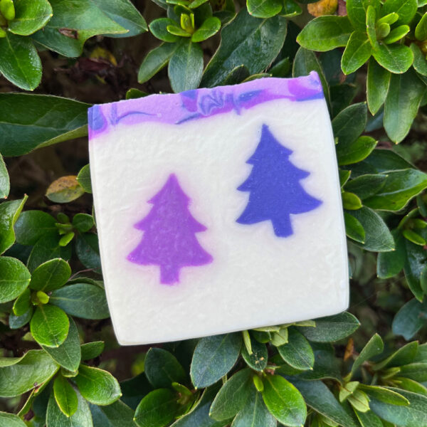 A Lavender soap with a purple christmas tree design, with dark green foliage in the background