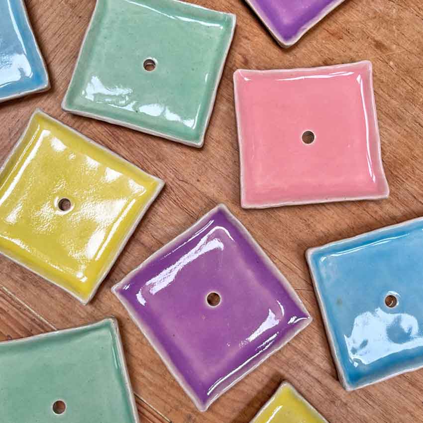 A flat lay showing square ceramic soap dishes in a variety of colours on a wooden tabletop