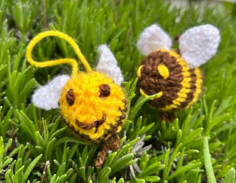 Two knitted bee lavender sachets hanging on a green lavender bush