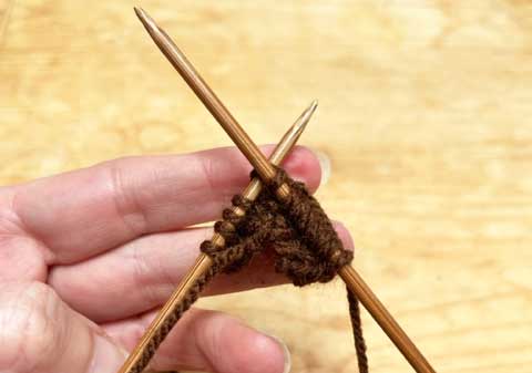 A pair of bamboo knitting needles and the first few rows of brown knitting, with a row half completed
