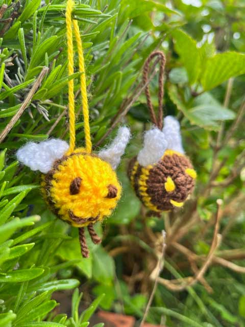 Two knitted lavender bees hanging in a green lavender bush