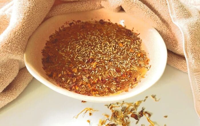 A white bowl filled with lavender infused water, displayed with a linen towel and calendula petals