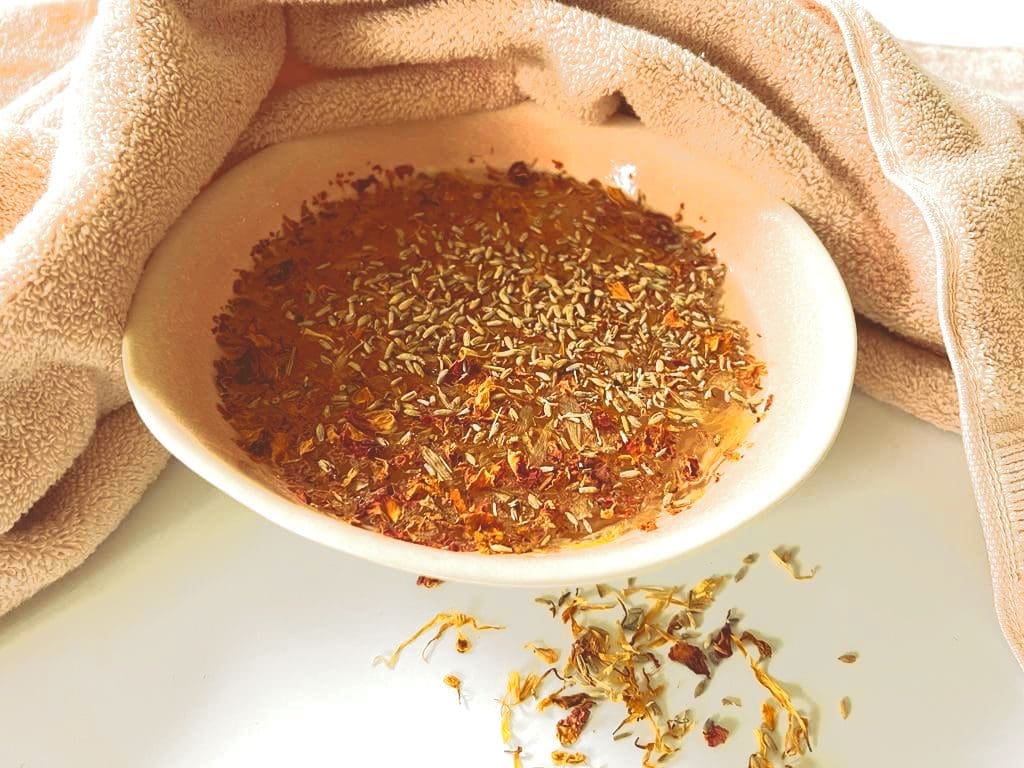 A white bowl filled with lavender infused water, displayed with a linen towel and calendula petals