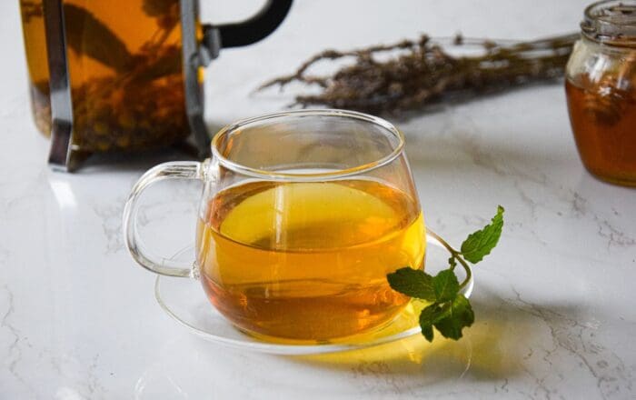 A glass mug containing chamomile, lavender and mint tea decorated with a sprig of mint