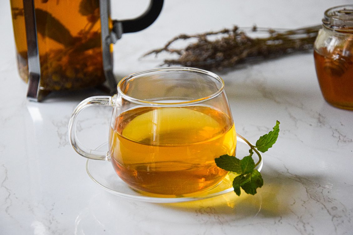 A glass mug containing chamomile, lavender and mint tea decorated with a sprig of mint