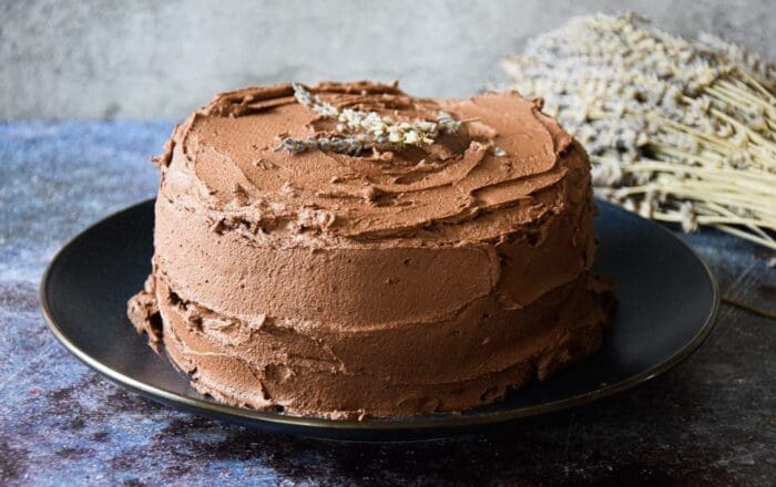 A chocolate cake with buttercream icing, decorated with a sprig of lavender