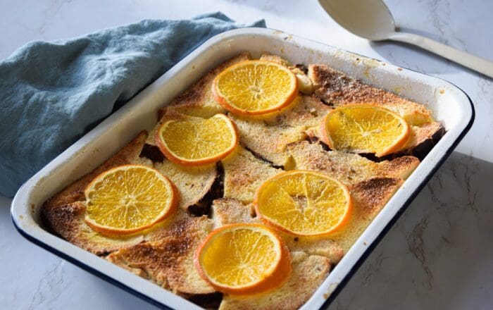 orange and lavender bread and butter pudding, served in a rectangular oven dish decorated with slices of orange