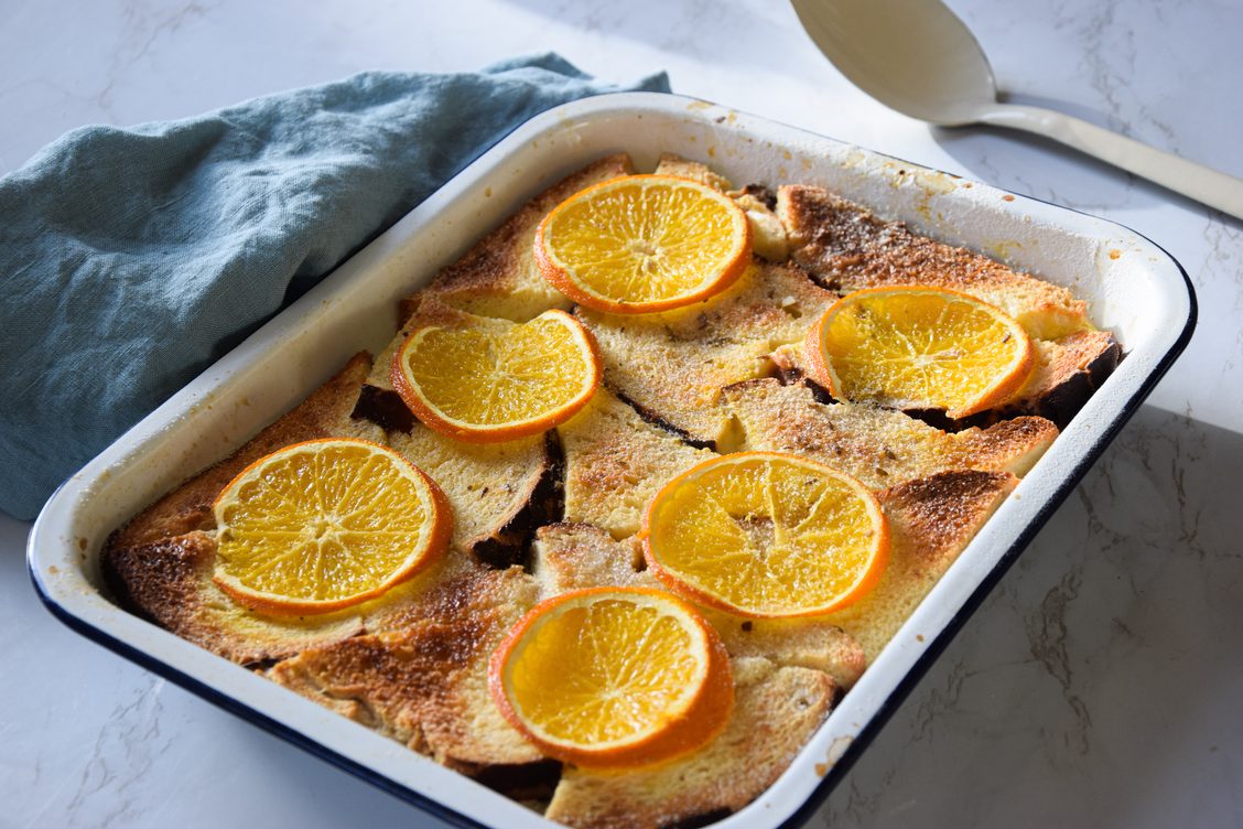 orange and lavender bread and butter pudding, served in a rectangular oven dish decorated with slices of orange