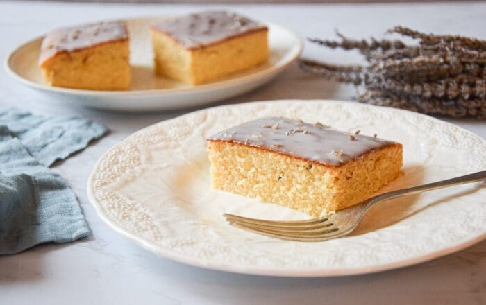 A slice of lavender rose traybake cake served on a white plate with a silver fork