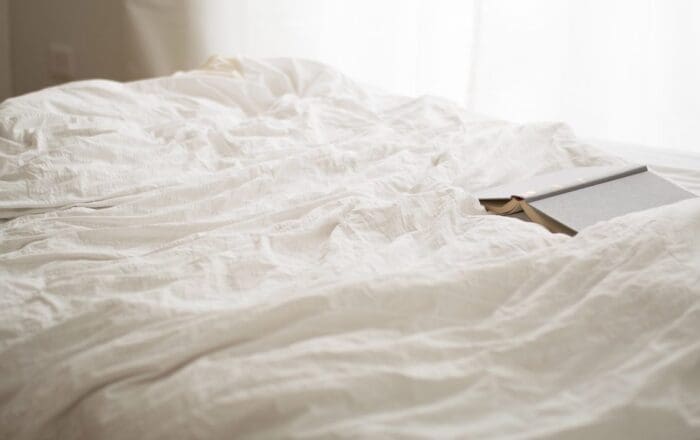 a bed with rumpled white sheets and a book left open on the duvet