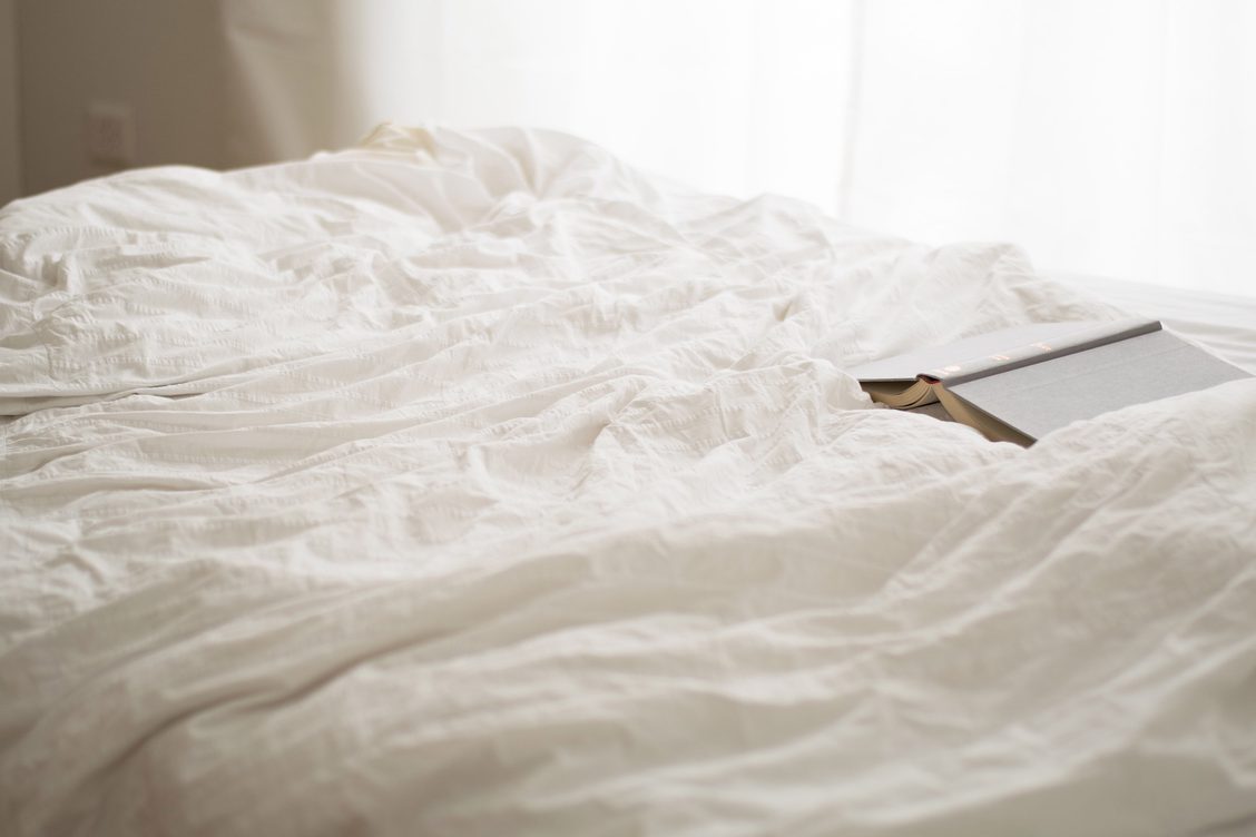 a bed with rumpled white sheets and a book left open on the duvet