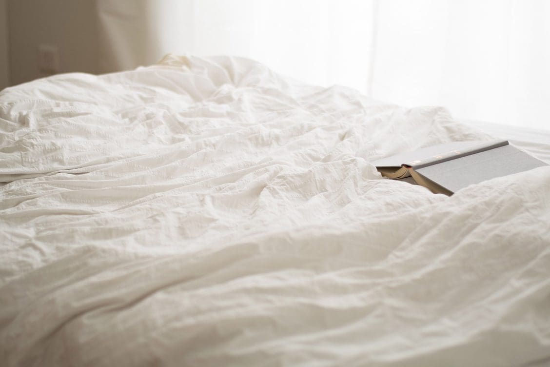 a bed with rumpled white sheets and a book left open on the duvet