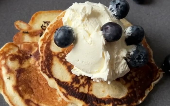A stack of lavender pancakes on a dark grey plate, topped with sugared cream and blueberries