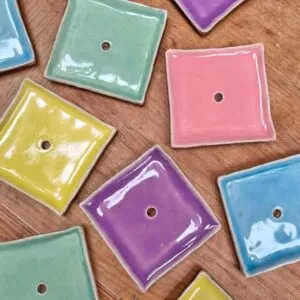 A flat lay showing square ceramic soap dishes in a variety of colours on a wooden tabletop